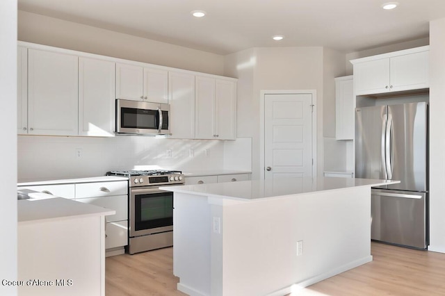 kitchen with stainless steel appliances, light countertops, backsplash, light wood-style floors, and white cabinetry