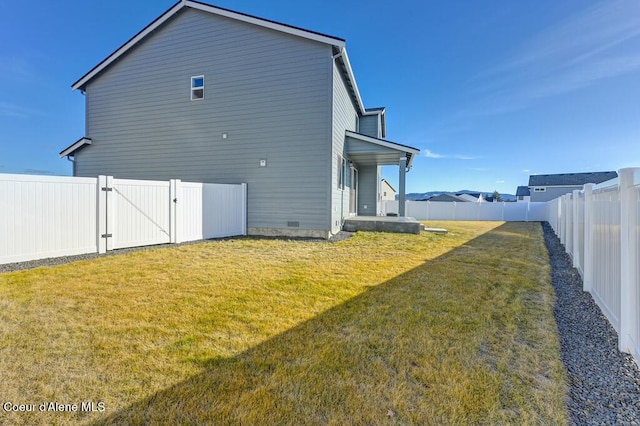 rear view of property featuring a lawn, a fenced backyard, and a gate