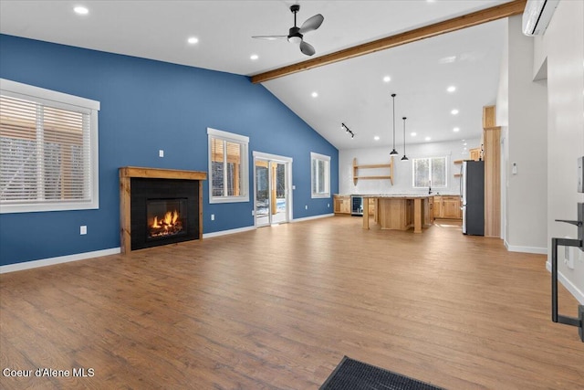 unfurnished living room featuring a ceiling fan, a glass covered fireplace, light wood-type flooring, beamed ceiling, and baseboards