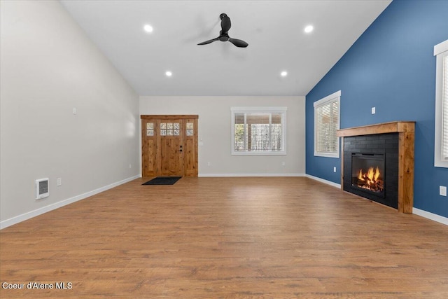 unfurnished living room with recessed lighting, vaulted ceiling, a glass covered fireplace, and wood finished floors