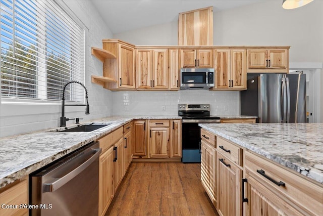 kitchen featuring light stone counters, a sink, stainless steel appliances, decorative backsplash, and wood finished floors