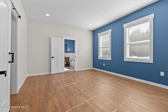 unfurnished bedroom featuring connected bathroom, a barn door, recessed lighting, baseboards, and wood finished floors