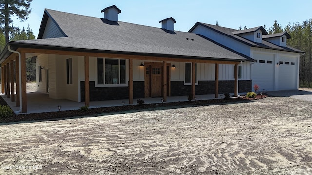 view of front facade featuring a shingled roof, an attached garage, stone siding, board and batten siding, and driveway