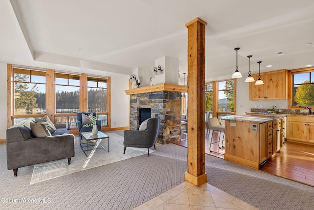 living area with a fireplace, light tile patterned floors, ornate columns, light colored carpet, and baseboards