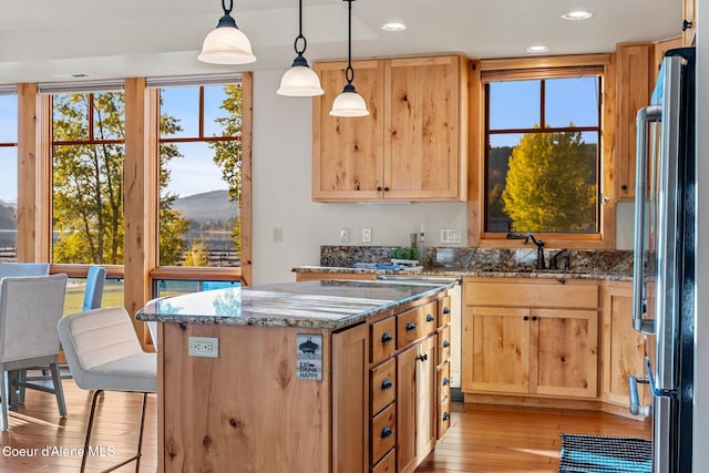 kitchen featuring stone counters, light wood-style flooring, a sink, and freestanding refrigerator