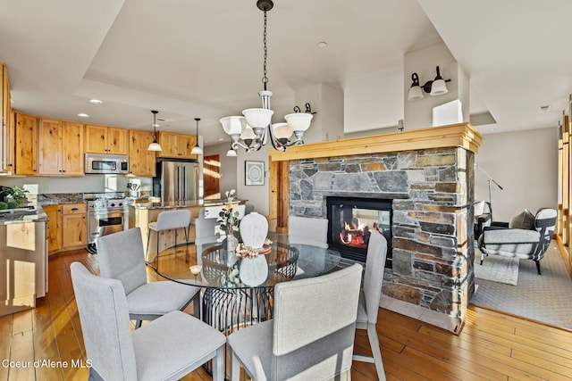 dining room with hardwood / wood-style flooring, recessed lighting, a fireplace, and an inviting chandelier