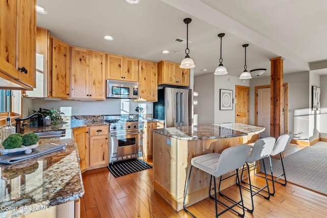 kitchen featuring premium appliances, a center island, light wood finished floors, a sink, and a kitchen breakfast bar