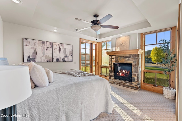 bedroom with a tray ceiling, carpet, visible vents, a ceiling fan, and a stone fireplace