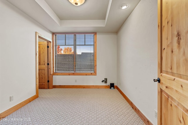 spare room with a tray ceiling, carpet flooring, and baseboards