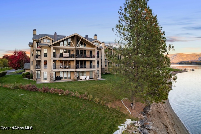 back of property at dusk featuring a patio area, a lawn, a water view, and a balcony