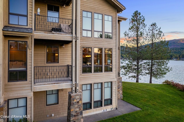 back of property at dusk featuring a balcony and a lawn