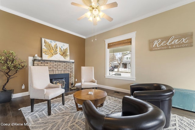 sitting room with ornamental molding, a ceiling fan, a brick fireplace, wood finished floors, and baseboards