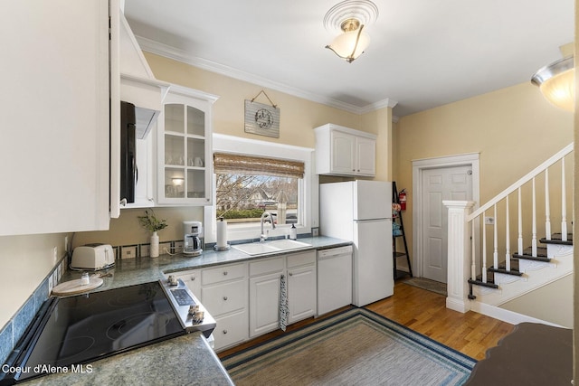 kitchen with glass insert cabinets, white cabinetry, a sink, wood finished floors, and white appliances