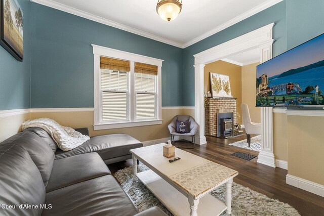 living area with baseboards, wood finished floors, crown molding, ornate columns, and a fireplace