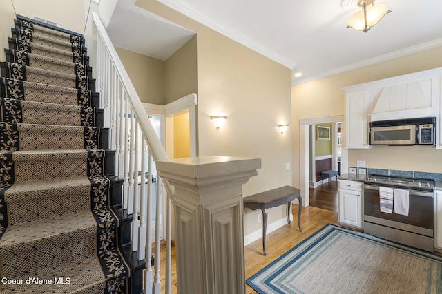 kitchen with baseboards, white cabinets, ornamental molding, appliances with stainless steel finishes, and light wood-type flooring