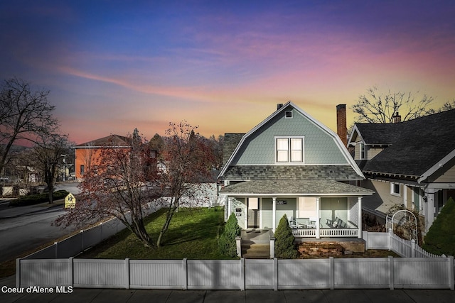 view of front of house featuring a porch, a fenced front yard, a shingled roof, a gambrel roof, and a lawn