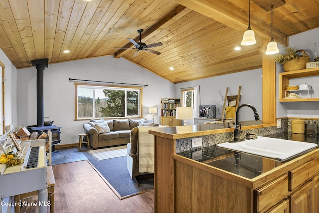 kitchen with a sink, lofted ceiling with beams, open floor plan, wooden ceiling, and a wood stove