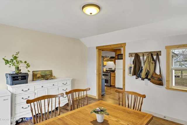 dining area with baseboards, light wood-style flooring, and vaulted ceiling