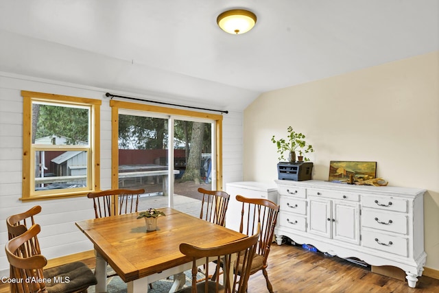 dining room with wood walls, vaulted ceiling, and light wood finished floors