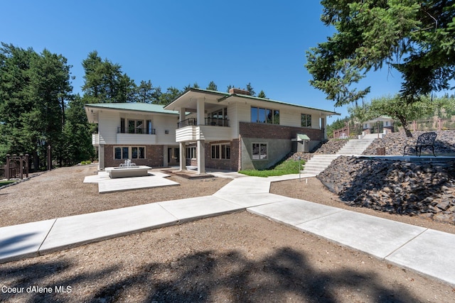 view of front of house with stairway, a patio area, brick siding, and a balcony