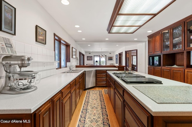 kitchen with cooktop, dishwasher, a peninsula, light wood-type flooring, and a sink