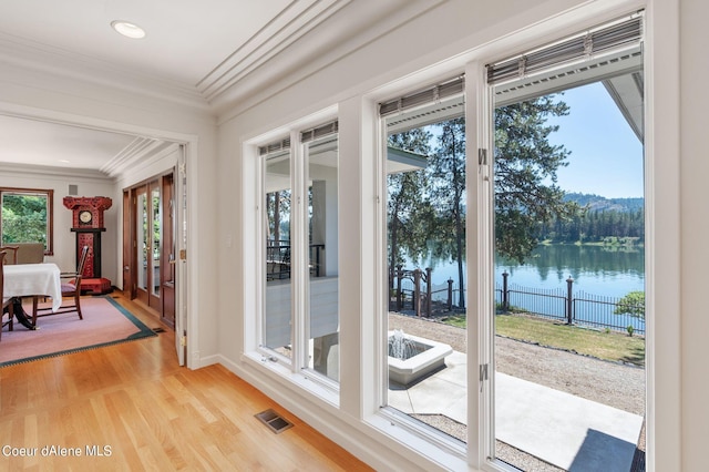 doorway with light wood-type flooring, a water view, visible vents, and crown molding