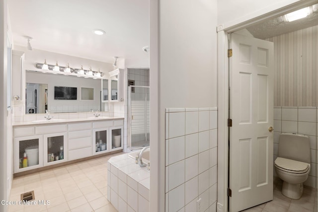 bathroom featuring double vanity, a stall shower, tile walls, and a sink