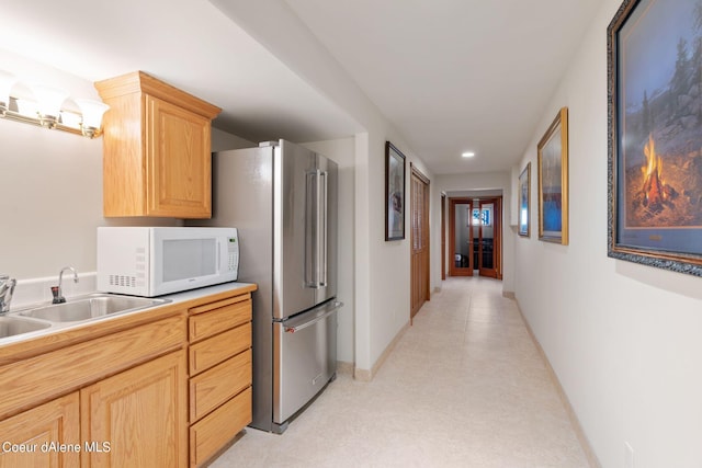 kitchen with white microwave, light brown cabinets, a sink, baseboards, and freestanding refrigerator