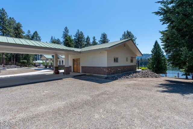 view of property exterior with driveway, fence, metal roof, and brick siding