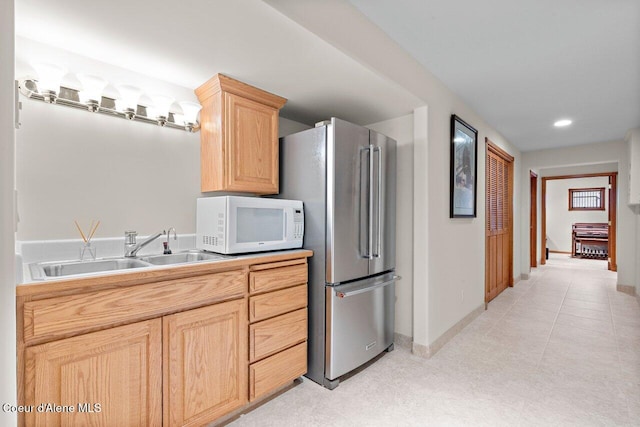 kitchen with freestanding refrigerator, light brown cabinetry, baseboards, white microwave, and a sink