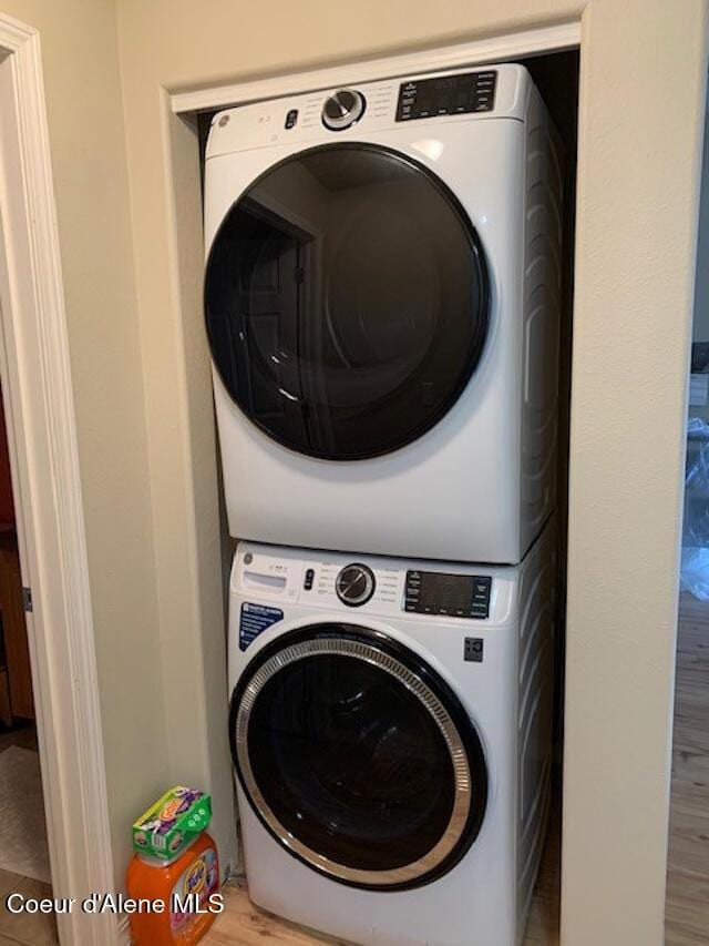 clothes washing area with laundry area, wood finished floors, and stacked washer and clothes dryer