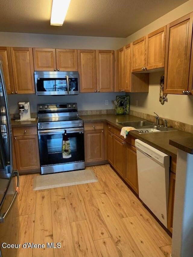 kitchen with dark countertops, light wood-style flooring, appliances with stainless steel finishes, brown cabinetry, and a sink