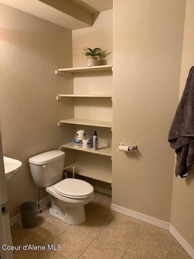 half bath with toilet, baseboards, and tile patterned floors