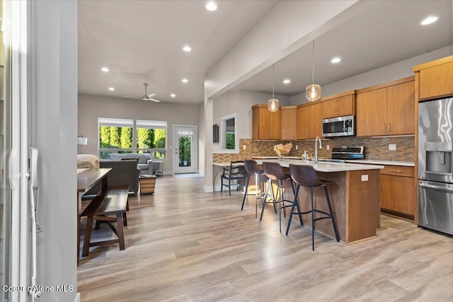 kitchen featuring appliances with stainless steel finishes, brown cabinets, light countertops, a kitchen bar, and backsplash