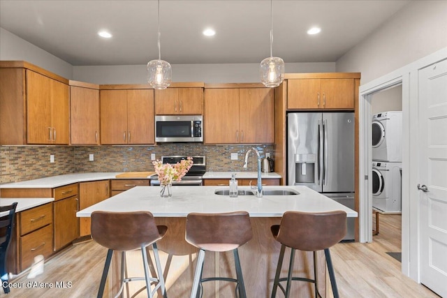 kitchen featuring light wood-style flooring, stainless steel appliances, stacked washer / dryer, a sink, and light countertops