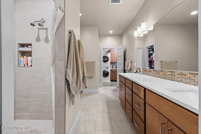 full bathroom featuring a walk in shower, tasteful backsplash, a sink, and stacked washer / drying machine