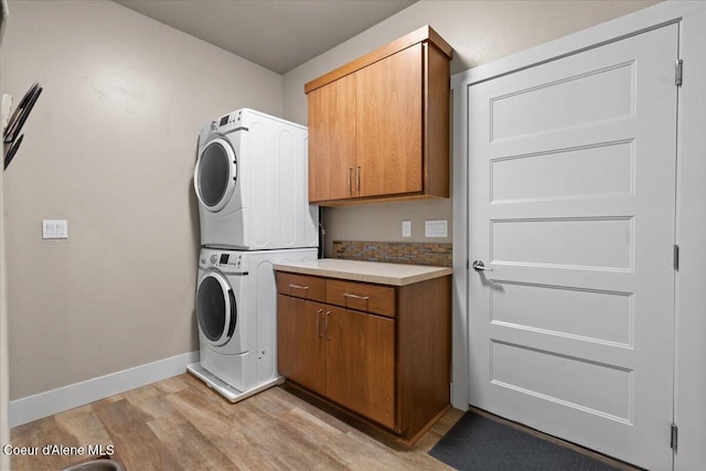 laundry area with baseboards, light wood-style flooring, cabinet space, and stacked washer / drying machine