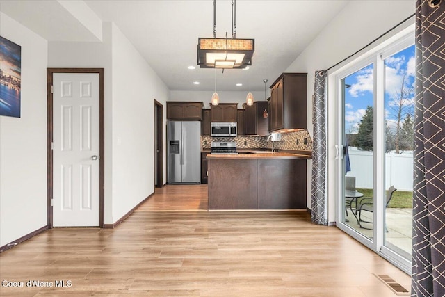 kitchen with pendant lighting, stainless steel appliances, light wood finished floors, decorative backsplash, and dark brown cabinets