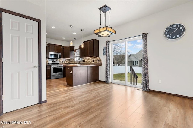 kitchen with stainless steel appliances, decorative backsplash, dark brown cabinetry, hanging light fixtures, and light wood-style floors