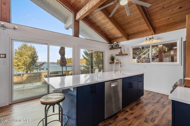 kitchen with light countertops, stainless steel dishwasher, a kitchen island with sink, a healthy amount of sunlight, and a sink