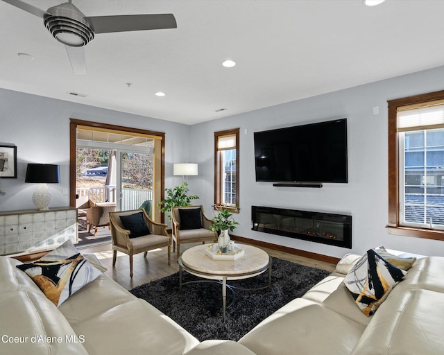 living area with wood finished floors, a wealth of natural light, and a glass covered fireplace