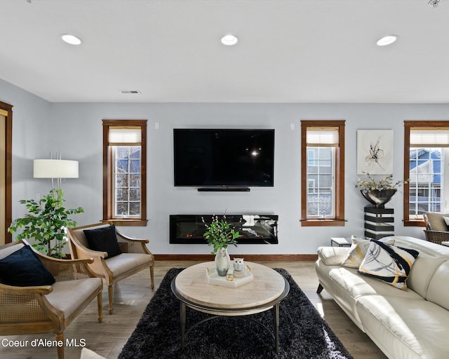 living area with baseboards, wood finished floors, a glass covered fireplace, and recessed lighting