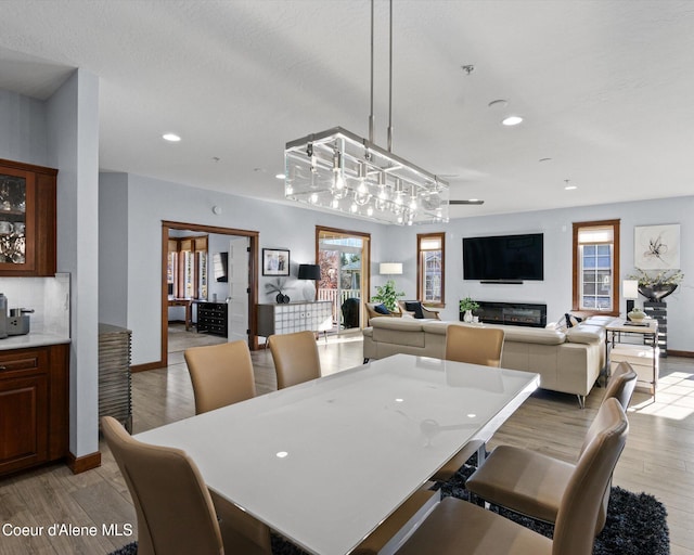 dining area with light wood-style floors, baseboards, a glass covered fireplace, and recessed lighting