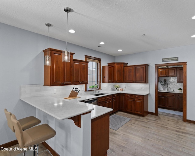 kitchen featuring a breakfast bar area, a peninsula, a sink, light countertops, and light wood-type flooring