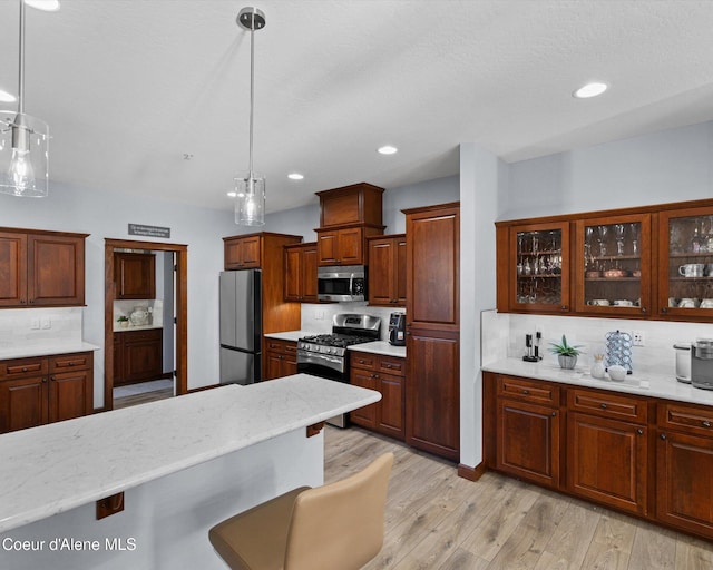 kitchen with recessed lighting, stainless steel appliances, hanging light fixtures, light wood finished floors, and glass insert cabinets