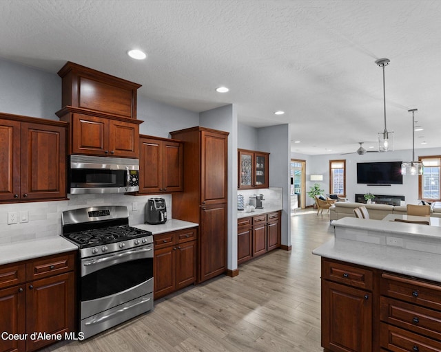 kitchen with light wood finished floors, stainless steel appliances, light countertops, backsplash, and open floor plan