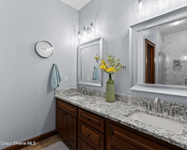 full bath featuring wood finished floors, a sink, a marble finish shower, and double vanity