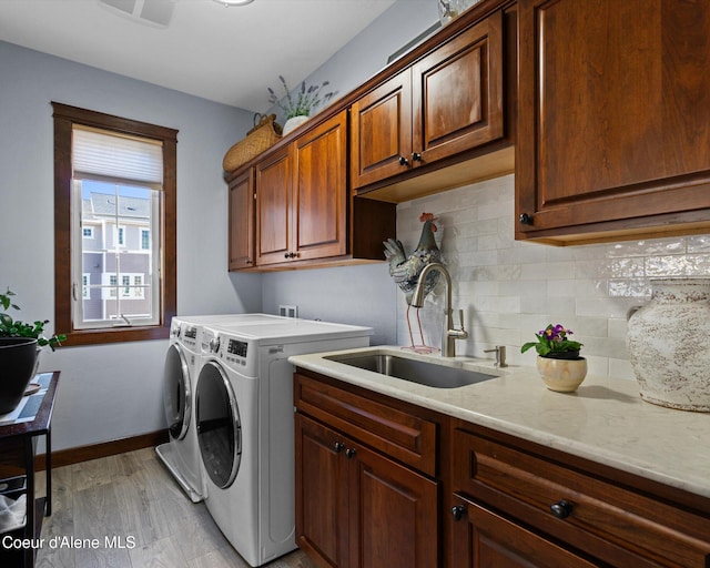 laundry area featuring cabinet space, baseboards, washing machine and clothes dryer, light wood-style floors, and a sink