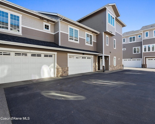 townhome / multi-family property with stone siding, driveway, and an attached garage