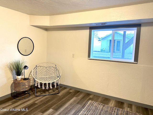 sitting room with a textured ceiling, baseboards, wood finished floors, and a textured wall